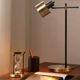 "Iron and brass table lamp with sleek, modern design, rotatable head, and sturdy base, placed on a desk with a vintage hourglass"