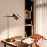 "Iron and brass table lamp with rotatable head, placed on a modern desk with books and decorative items, perfect for workspaces"