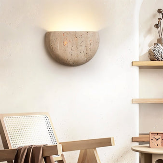 "A minimalist, semi-circular travertine wall lamp sconce emitting a soft glow in a modern bedroom."