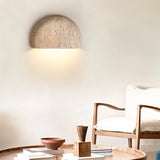 "A minimalist, semi-circular travertine wall lamp enhancing a modern living room with its soft glow and organic texture."