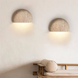 "Pair of minimalist, semi-circular travertine wall lamps flanking a modern sofa, providing soft, ambient lighting."