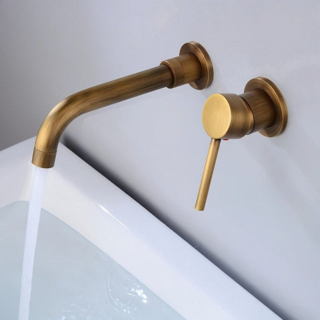 Antique brass Vartay Bathroom Faucet with water flowing, wall mounted above a modern white basin.