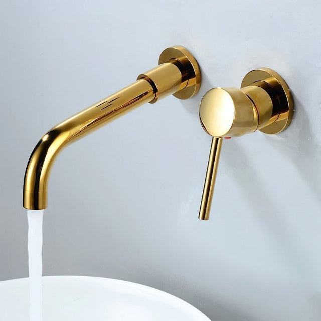 Gold Vartay Bathroom Faucet in use, wall mounted above a white basin with water flowing from the curved spout.