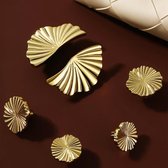 "Gold brass fan-shaped drawer pulls arranged on a dark red surface."