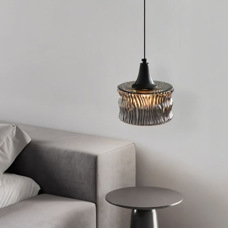 "A pendant light with a rippled glass shade beside a bedroom side table."