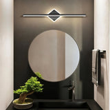 "A modern black wall lamp with a diamond-shaped base and horizontal bar, mounted above a round mirror in a contemporary bathroom with a dark accent wall."