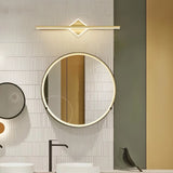 "A modern gold wall lamp with a diamond-shaped base and horizontal bar, mounted above a round mirror in a contemporary bathroom with textured walls."