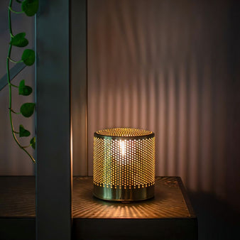 "A brass table lamp with a perforated metal body emitting a soft light on a nightstand with a dark background."