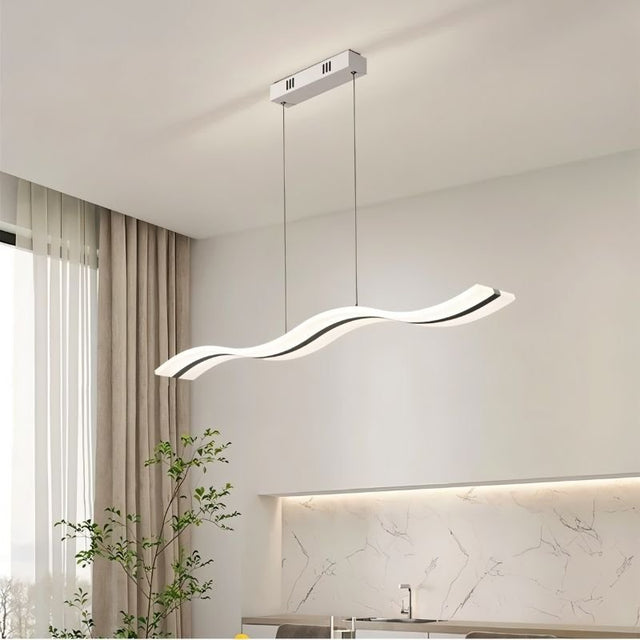 "A modern LED pendant light with an undulating wave design, illuminating a kitchen with white countertops and a plant."