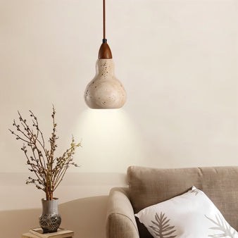 "A travertine pendant light hanging in a living room with a sofa and vase."