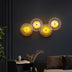 Five illuminated circular wall lamps with golden-yellow glass and metallic frames arranged in a wave pattern on a dark wall.