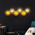 Six glowing golden circular wall lamps with radiating wire frames mounted on a dark wall above modern seating.