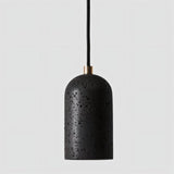 "Modern cylindrical pendant light in black travertine with brass detailing, showcasing its natural, textured surface."