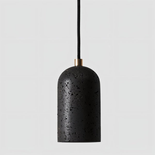 "Modern cylindrical pendant light in black travertine with brass detailing, showcasing its natural, textured surface."