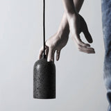 "Person holding a modern cylindrical pendant light crafted from black travertine, showcasing its natural, textured surface and contemporary design."