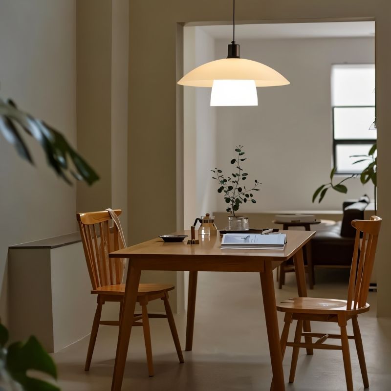 "A layered glass pendant light hanging above a wooden dining table with chairs in a modern dining room."