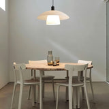 "A layered glass pendant light hanging above a round table with white chairs in a minimalist dining room."
