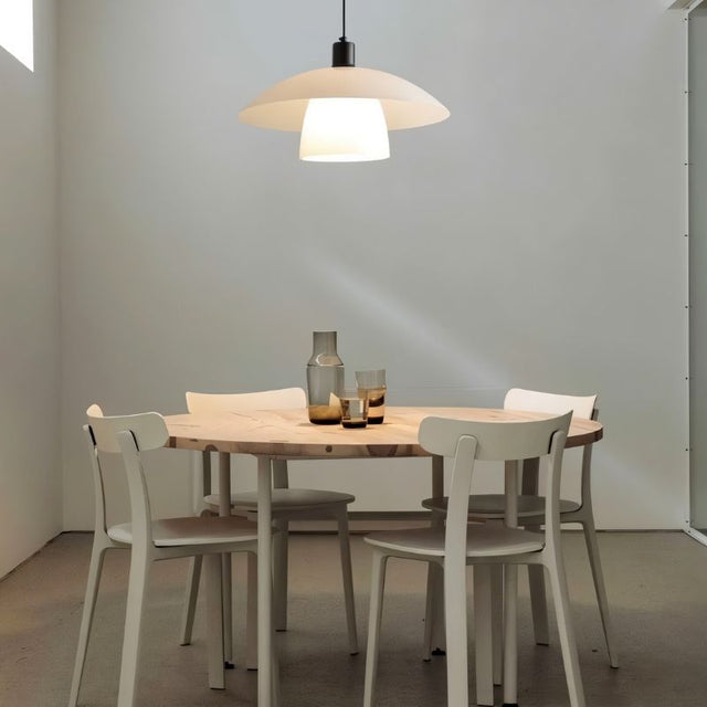 "A layered glass pendant light hanging above a round table with white chairs in a minimalist dining room."