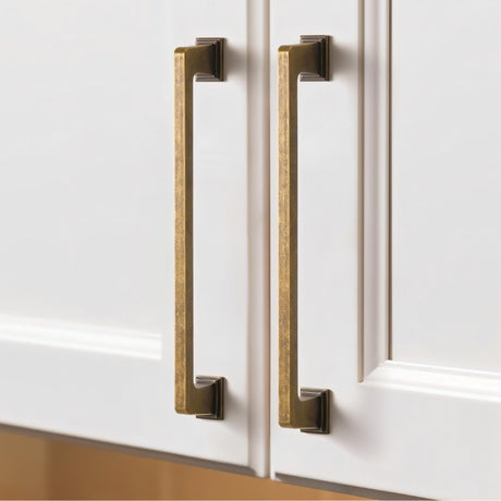 "Two vintage brass pull bars with a sleek, modern rectangular design, installed on white kitchen cabinets, offering a luxurious and functional touch."