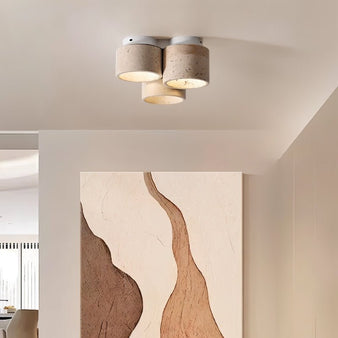 "Triple cylinder yellow travertine ceiling light with iron base above modern artwork, warm interior lighting."