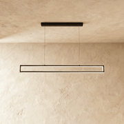 Linear bronze pendant light with warm LED glow suspended from black ceiling canopy over dining table in studio setting.