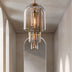 Stacked glass cylinder pendant lights with brushed brass frame in neutral hallway setting.