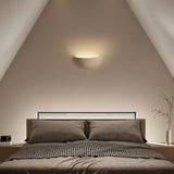 "Sleek, minimalist, half-moon shaped trimless light made of gypsum and metal, recessed into a bedroom wall, providing a soft, ambient glow above a modern bed with built-in headboard lighting."