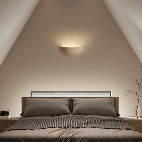 "Sleek, minimalist, half-moon shaped trimless light made of gypsum and metal, recessed into a bedroom wall, providing a soft, ambient glow above a modern bed with built-in headboard lighting."