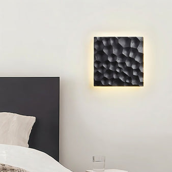 "Close-up of a black travertine wall lamp with hexagonal pattern, backlit glow, mounted on a bedroom wall."