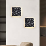 "Two black travertine wall lamps with hexagonal patterns, backlit glow, mounted on a living room wall with modern decor."