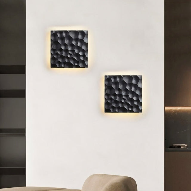 "Two black travertine wall lamps with hexagonal patterns, backlit glow, mounted on a living room wall with modern decor."