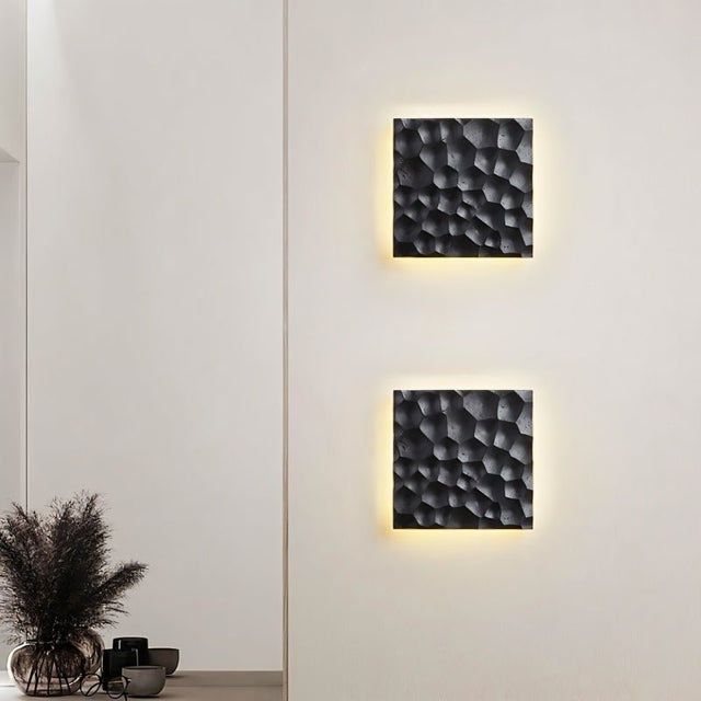 "Two black travertine wall lamps with hexagonal patterns, backlit glow, mounted on a wall in a modern interior."