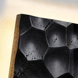 "Extreme close-up of a black travertine wall lamp showing the hexagonal pattern and textured surface."