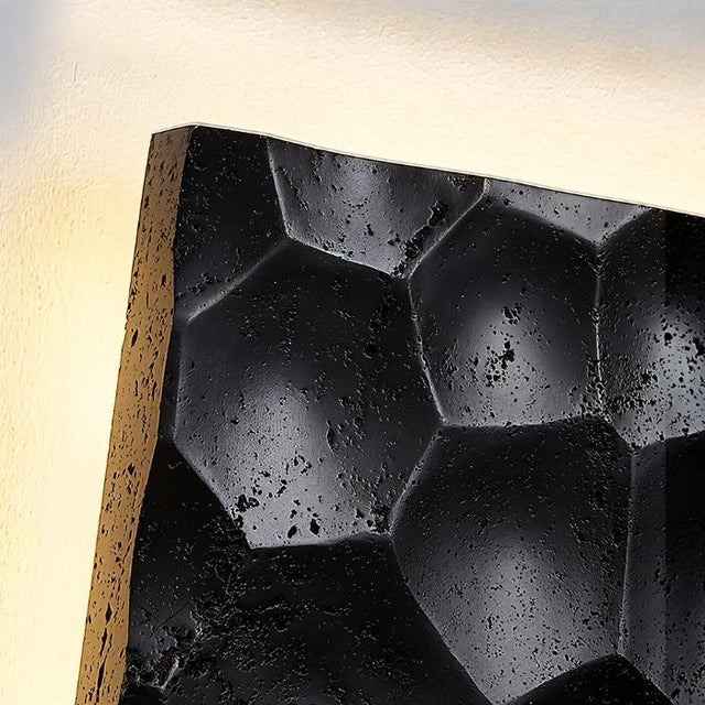 "Extreme close-up of a black travertine wall lamp showing the hexagonal pattern and textured surface."