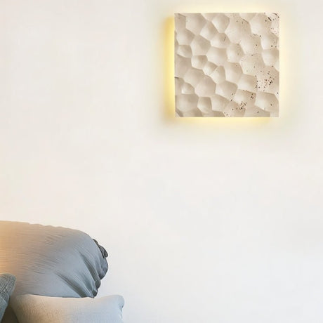 "A close-up of a square travertine wall lamp with a textured hexagonal surface, mounted on a white wall, emitting a soft glow."