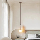 "Cylindrical travertine pendant light with a frosted glass diffuser, hanging in a bedroom with a textured wall."