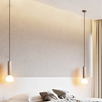 "Two cylindrical travertine pendant lights with frosted glass diffusers, hanging above a bed."