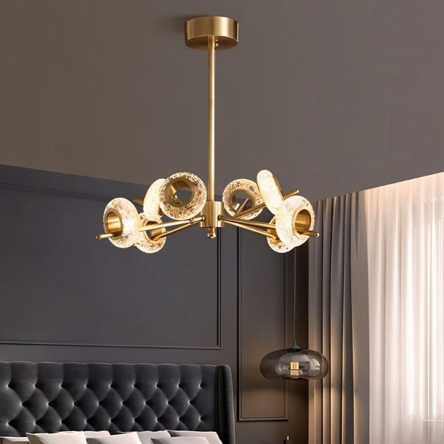 "A modern chandelier with circular glass accents and a gold metal frame in a contemporary bedroom."