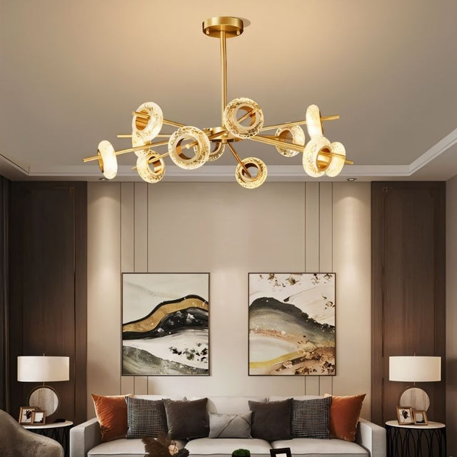 "A modern chandelier with circular glass accents and a gold metal frame hanging above a sofa with two framed artworks."