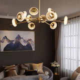 "A modern chandelier with circular glass accents and a gold metal frame above a sofa with artwork in a living room."