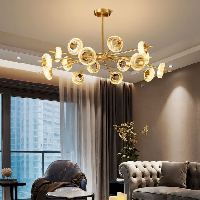 "A modern chandelier with circular glass accents and a gold metal frame in a living room with a city view."