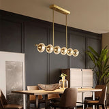"A modern linear chandelier with circular glass accents and a gold metal frame hanging above a dining table in a well-decorated dining room."