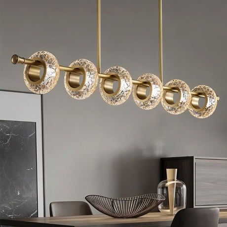 "A modern linear chandelier with circular glass accents and a gold metal frame above a dining table."