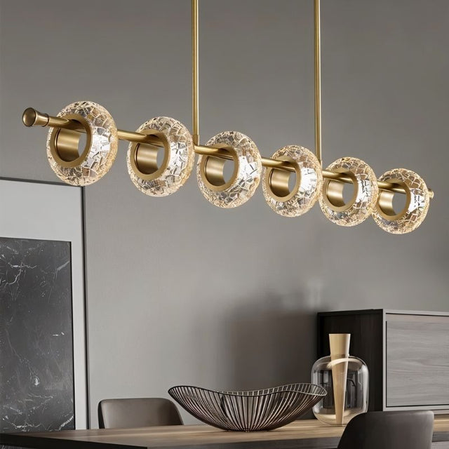 "A modern linear chandelier with circular glass accents and a gold metal frame above a dining table."