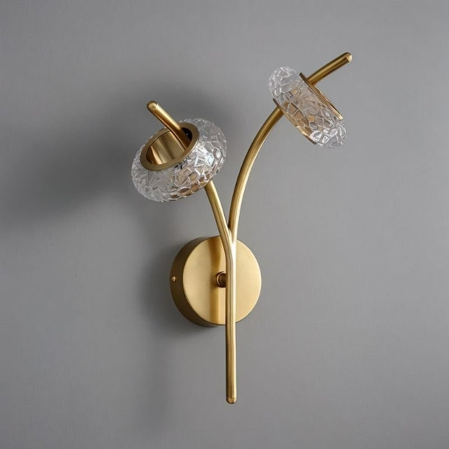 "A modern wall lamp with two clear textured glass shades and a gold metal frame, mounted on a gray wall."