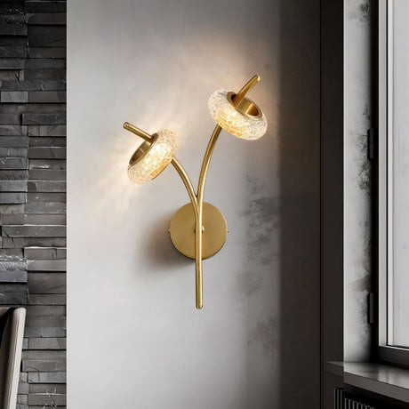 "A modern wall lamp with two textured glass shades and a gold metal frame, mounted on a textured wall."