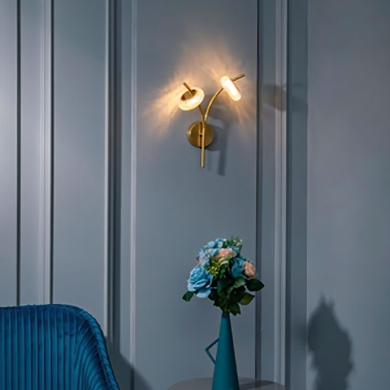 "A modern wall lamp with two glass shades and a gold metal frame mounted on a gray paneled wall."