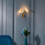 "A modern wall lamp with two glass shades and a gold metal frame mounted on a gray paneled wall."
