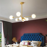 "A gold chandelier with eight frosted glass globes, hanging in a bedroom with a blue tufted headboard."