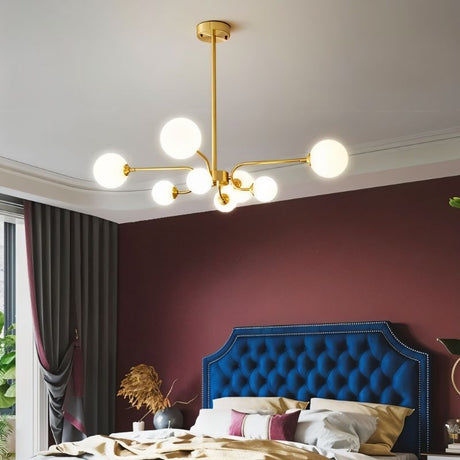 "A gold chandelier with eight frosted glass globes, hanging in a bedroom with a blue tufted headboard."